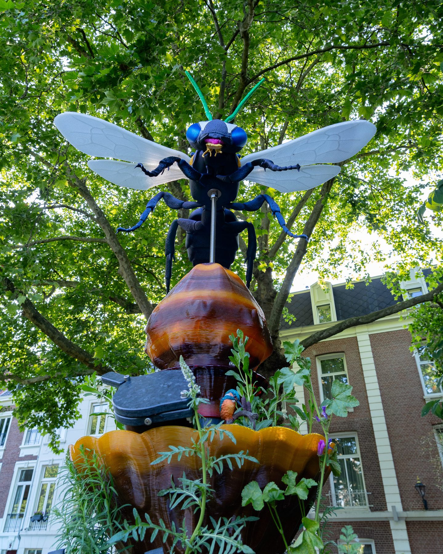 Een BeeTotem met een grote houten wilde bij, tussen bomen en gevels in Amsterdam